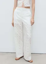 Pantalón blanco de algodón con bordado floral, tiro medio, diseño recto, detalles calados y cierre frontal oculto con botón, gancho y cremallera.