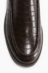 Mocasines marrones con textura de piel de cocodrilo, costura tradicional en la parte delantera, forro de lona de algodón y suela de goma. Tacón de 1 cm.