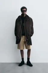 Trench relaxed fit negro confeccionado en tejido técnico ligeramente acolchado, con cuello subido y capucha desmontable. Tiene manga larga, bolsillos de vivo en pecho y de solapa en cadera, y abertura en el centro de la espalda. El cierre frontal es con cremallera oculta por solapa con botones a presión.