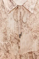 Camisa con estampado animal print en tonos beige y marrón, con cuello solapa y escote pico. Manga larga con capas en mismo tejido y bajo acabado en volantes. Cierre frontal con botones y lazada.