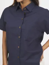 Camisa azul marino de lino y algodón, con cuello clásico, mangas cortas con dobladillo, cierre frontal con botones de madera y bolsillo de parche en el pecho.