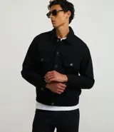 Campera trucker masculina de jeans negro, con cuello inglés, manga larga ajustada, cierre abotonado, bolsillos delanteros y sin estampa.