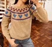 Sweater tejido a mano en mohair color beige con cuello redondo y mangas largas abullonadas. Presenta un diseño geométrico en el canesú con rombos color lila y corazones color azul.