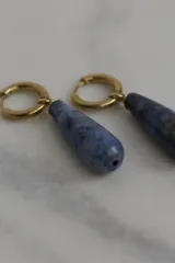 Par de aros colgantes con argolla dorada de acero quirúrgico y dije de piedra natural azul en forma de gota.
