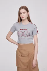 Remera gris de corte cropped con estampado de texto "New York USA" en color rojo y ribetes rojos en las mangas.