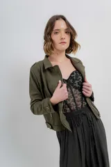 Chaqueta verde militar de gamuza sintética con elastano, cuello solapa, manga larga con trabillas en los hombros, bolsillos frontales con cremallera metálica y cierre frontal con cremallera.