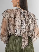 Camisa de seda italiana con estampado sutil de animal print en tonos tierra y beige. Diseño reversible con lazo que puede usarse en la espalda o al frente. Presenta volados en los hombros y mangas largas.