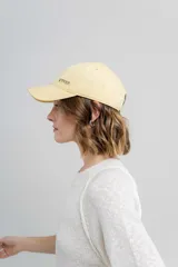 Gorra de béisbol color amarillo pastel, con visera curva y logo de Peach bordado en el frente. Ajustable en la parte trasera.