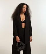 Blazer negro de poliéster y elastano, corte sastrero alargado, con cuello solapa y mangas largas con pliegues.