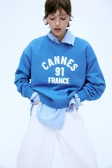 Buzo azul con cuello redondo, puños y bajo acanalados. Estampado frontal con la leyenda "Cannes 91 France" en color blanco.