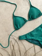 Conjunto de bikini verde esmeralda con textura acanalada. El corpiño es de triángulos movibles con tiras finas para atar al cuello y a la espalda, y tiene almohadillas desmontables. La bombacha es vedetina ancha con laterales fijos.