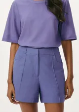 Short de vestir color lila, de corte recto, con bolsillos laterales y cierre frontal con botón y cremallera.
