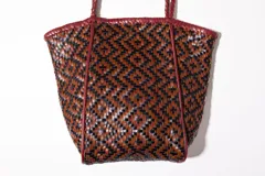 Bolso tote de cuero trenzado en tonos marrón y negro, con asas de cuero trenzado color bordó.