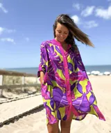 Vestido camisero de corte oversize con estampado de hojas tropicales en colores violeta, fucsia y verde. Presenta cuello mao, cierre frontal con botones y mangas cortas holgadas.