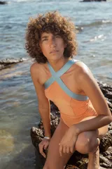 Traje de baño entero color naranja con breteles cruzados en color celeste.