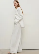 Pantalón de jeans blanco, tiro alto, corte wideleg (pierna ancha) y largo completo. Presenta cinco bolsillos y cierre frontal con botón y cremallera.