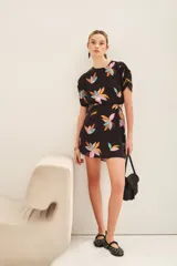 Vestido corto negro con estampado floral abstracto en tonos pastel (rosado, naranja, celeste, amarillo). Presenta cuello redondo, mangas cortas abullonadas y abertura horizontal en la cintura.