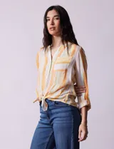 Blusa de gasa estampada a rayas verticales en tonos celeste, lila, naranja y marrón. Tiene cuello a la base con escote en V y botones. Delantera con bolsillo aplicado. Largo de manga regulable con presilla y botón. Terminación anudada opcional.