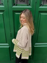 Sweater beige de tejido grueso con cuello alto, corte oversize y tajo a los lados. Tiene rayas horizontales verdes en el ruedo y en los puños.