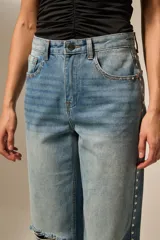 Pantalón jean negro con roturas en las rodillas, diseño de estrellas metálicas a lo largo de las costuras laterales y en los bolsillos delanteros.