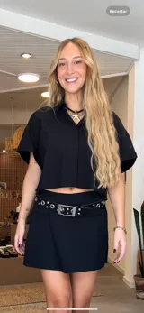 Minifalda negra con diseño cruzado y cinturón de cuero con hebilla metálica y ojalillos.