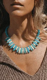 Collar corto con cuentas de piedra turquesa y colmillos de piedra fósil blanca.