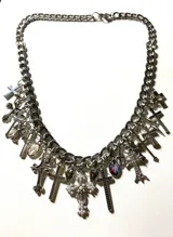 Collar plateado de cadena gruesa con dijes colgantes de cruces de diferentes estilos, corazones y camafeos.