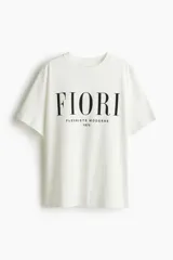 Remera blanca de corte holgado en punto de algodón. Modelo con cuello redondo y estampado frontal con la palabra 'FIORI' y la frase 'FLEURISTE MODERNE 1975' en color negro.
