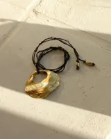 Collar con dije dorado en forma de concha marina y cordón marrón de seda natural.