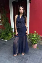 Falda larga de color azul marino confeccionada en microtul y gasa. Presenta un diseño con frunces y plisados en la zona de la cadera que brindan un ajuste al cuerpo, y una parte inferior fluida con transparencias y efecto godet.