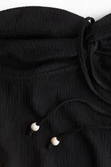 Top corto negro de punto con textura, corte entallado, escote halter y tiras finas con cuentas en los extremos.