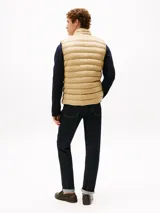 Chaleco acolchado color beige, con cuello chimenea y cierre frontal de cremallera. Presenta costuras horizontales y logo de Tommy Hilfiger bordado en el pecho.