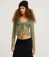 Blusa verde de encaje floral transparente, con escote en V y lazos delanteros.