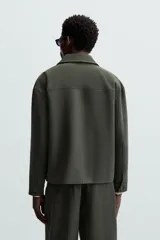 Sobrecamisa negra de corte amplio, con cuello solapa, manga larga con puños abotonados, bolsillos de parche en el pecho, bolsillos laterales y cierre frontal con botones.