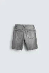 Bermuda de denim de algodón, color gris lavado, con corte relaxed fit y roturas visibles en la parte delantera de ambas piernas. Presenta cinco bolsillos y cierre frontal con cremallera y botón.