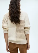 Sweater de punto grueso color beige con diseño patchwork. Tiene cuello alto y mangas largas.