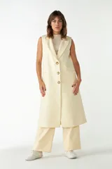 Chaleco largo color crema de lana fina sin mangas, con solapas y cierre frontal con tres botones. Presenta bolsillos ojal.