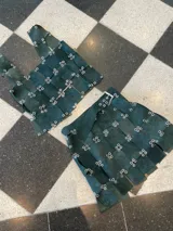 Falda corta de gamuza color verde inglés, con diseño tejido o trenzado a partir de tiras de material, sujetas con argollas metálicas plateadas. La pieza inferior parece tener un cinturón con hebilla plateada.