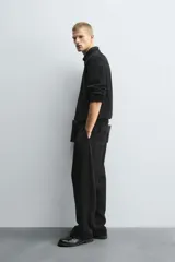 Pantalón negro de corte relajado con cintura elástica ajustable y pliegues en la parte delantera. Presenta bolsillos laterales y bolsillos traseros de parche.