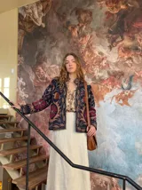 Chaqueta corta negra con bordados florales en tonos oro, carmín y arena. Tiene cuello mao y cierre frontal con broches.