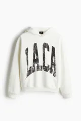 Canguro blanco con capucha forrada cruzada, bolsillo canguro y diseño estampado con letras negras. Corte holgado con hombros caídos y remate acanalado en puños y bajo.