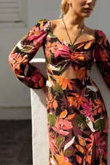Vestido midi con estampado floral en tonos lila, amarillo y verde. Tiene escote fruncido con lazo ajustable, mangas largas abullonadas y tajo lateral.