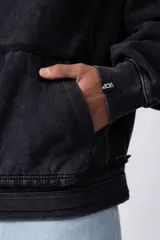 Buzo canguro negro con capucha, calce oversize, confeccionado en frisa 100% algodón con lavado gastado y aplique cosido en el pecho.