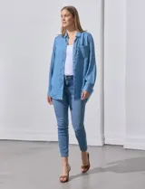 Camisa de jean celeste con flecos en el ruedo, de mangas largas y corte recto.