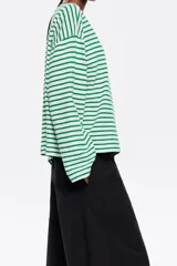Camiseta de algodón con estampado de rayas horizontales verdes y blancas, cuello redondo con ribete azul marino, mangas largas y logo bordado en el pecho.