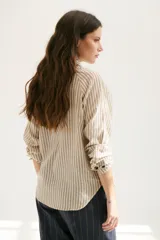 Camisa a rayas verticales color beige y blanco, con cuello clásico, botones marrones y mangas largas.