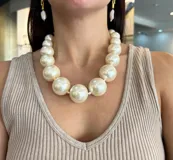 Collar corto de perlas de resina color crema, de tamaño grande y forma esférica, dispuestas de mayor a menor. Cierre de mosquetón dorado con cadena regulable.