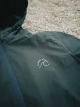 Campera verde oscuro con estampado de dibujos en blanco en el frente. Corte recto, con cierre frontal y bolsillos laterales con cierre.