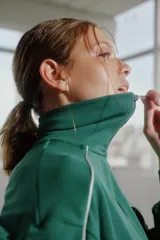 Campera deportiva verde con cierre frontal, cuello alto y detalles de vivos blancos en hombros y mangas.