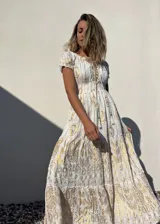 Vestido largo blanco con estampado dorado, escote en V con cordones y mangas cortas abullonadas.